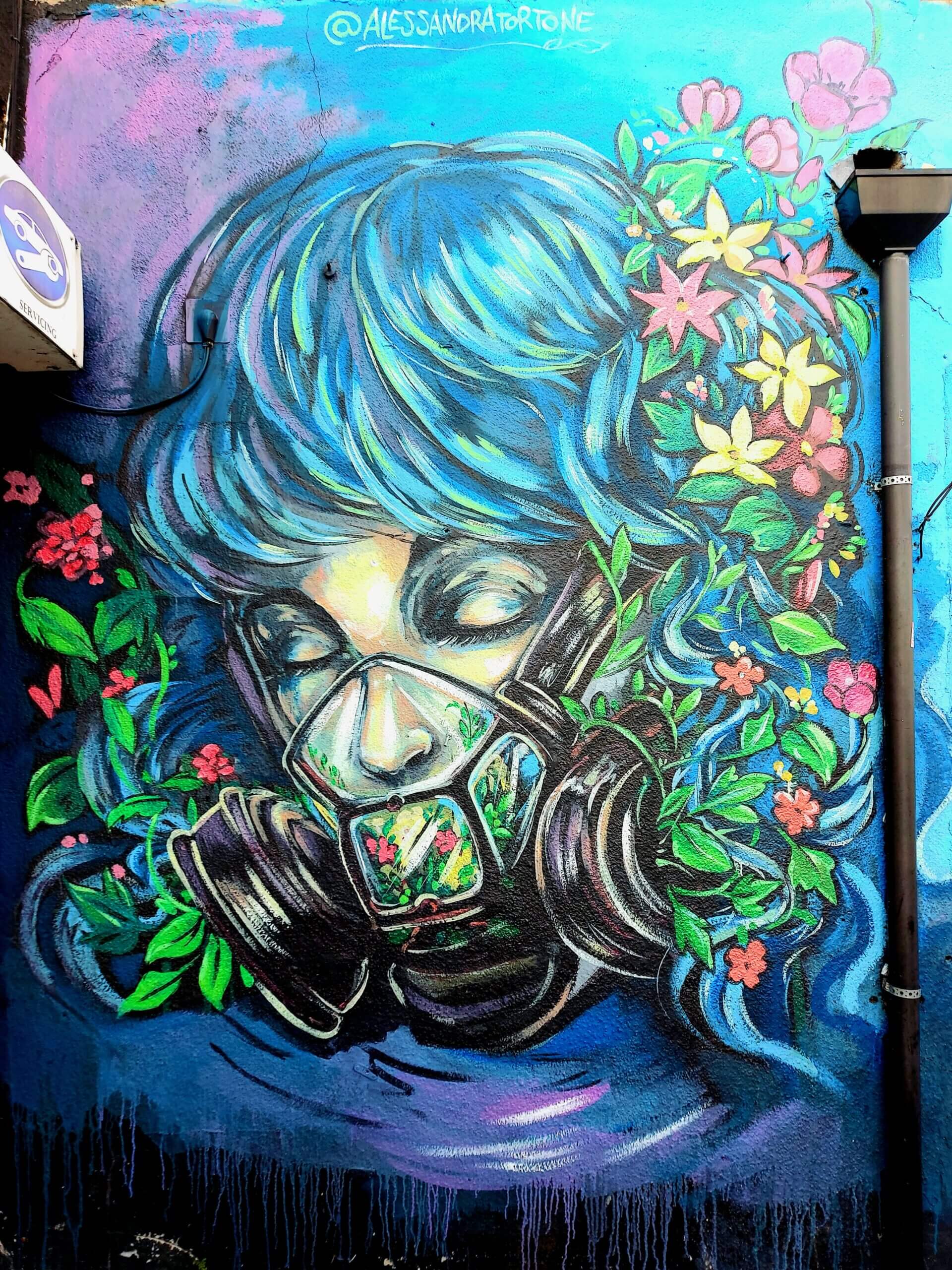 Street artwork of a female wearing a gas mask filled with flowers and exhaling flowers