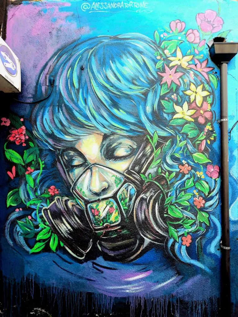 Graffiti street art mural of a female wearing a gas mask filled with flowers and exhaling flowers