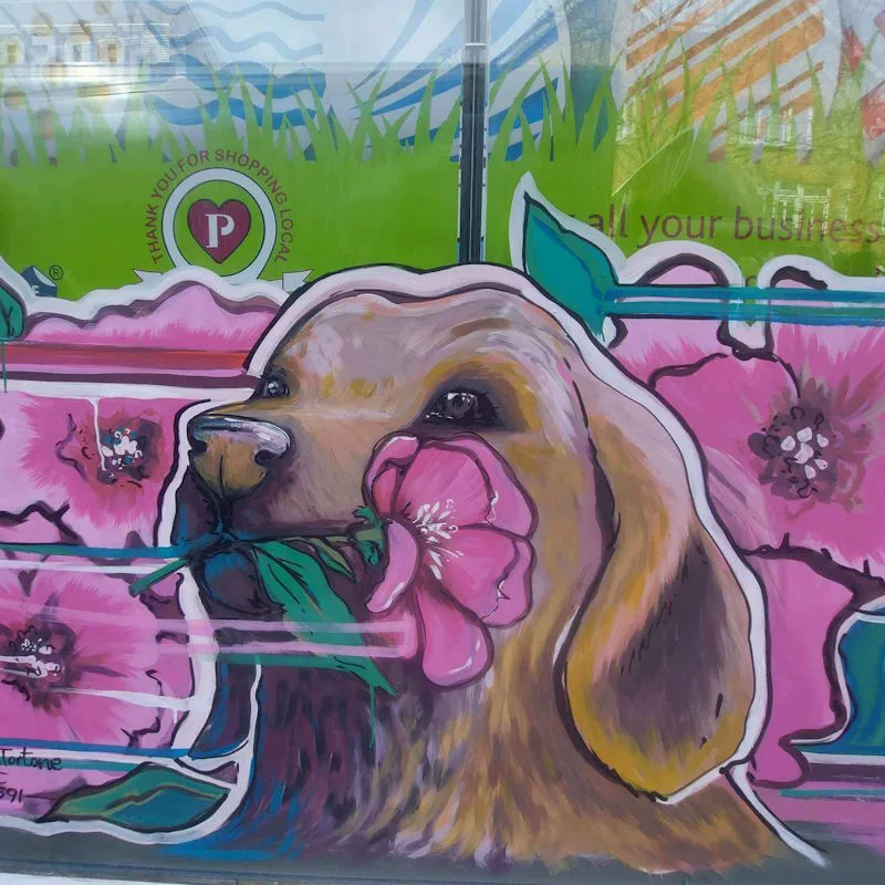 Hand painted window art of a dog holding a flower in its mouth.